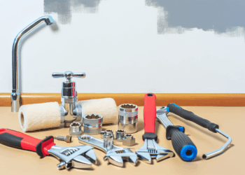 Domáca súprava na opravy na stole: kohútik, kľúče, valček, skrutkovače, zásuvky, stena s náterom.