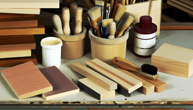 Dielňa s náradím na prácu s drevom, brúsky, štetce, nádoby na laky, kusy neopracovaného dreva.