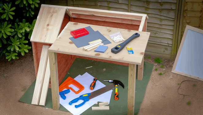 Materiály a nástroje na konštrukciu detského záhradného domčeka na pracovnom stole v záhrade.