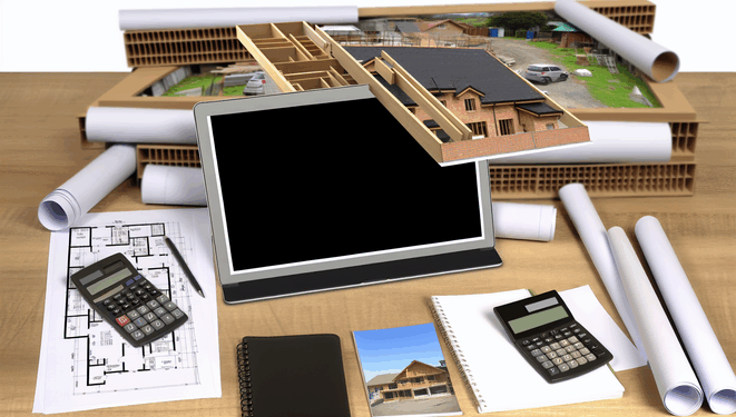 Stôl s plánmi, kalkulačkou, materiálovými vzorkami, notebookom, laptopom a výhľadom na stavbu domu.
